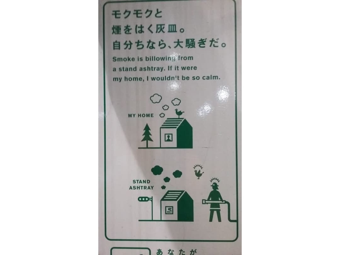 A sign that reads: Smoke is billowing from a stand ashtray. It it were my home, I wouldn't be so calm.
